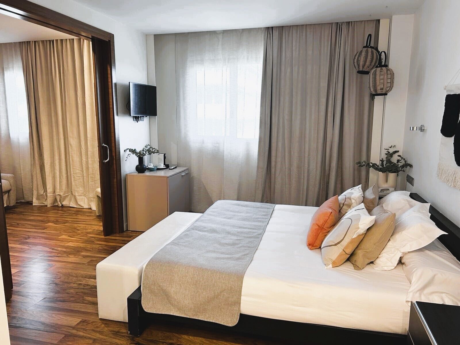A modern hotel room with a large bed, a bedside table with a lamp, a flat-screen TV, and a view of the hallway.