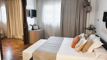 Habitación de hotel moderna con una cama grande, una mesita de noche con lámpara, un televisor de pantalla plana y vistas al pasillo.
