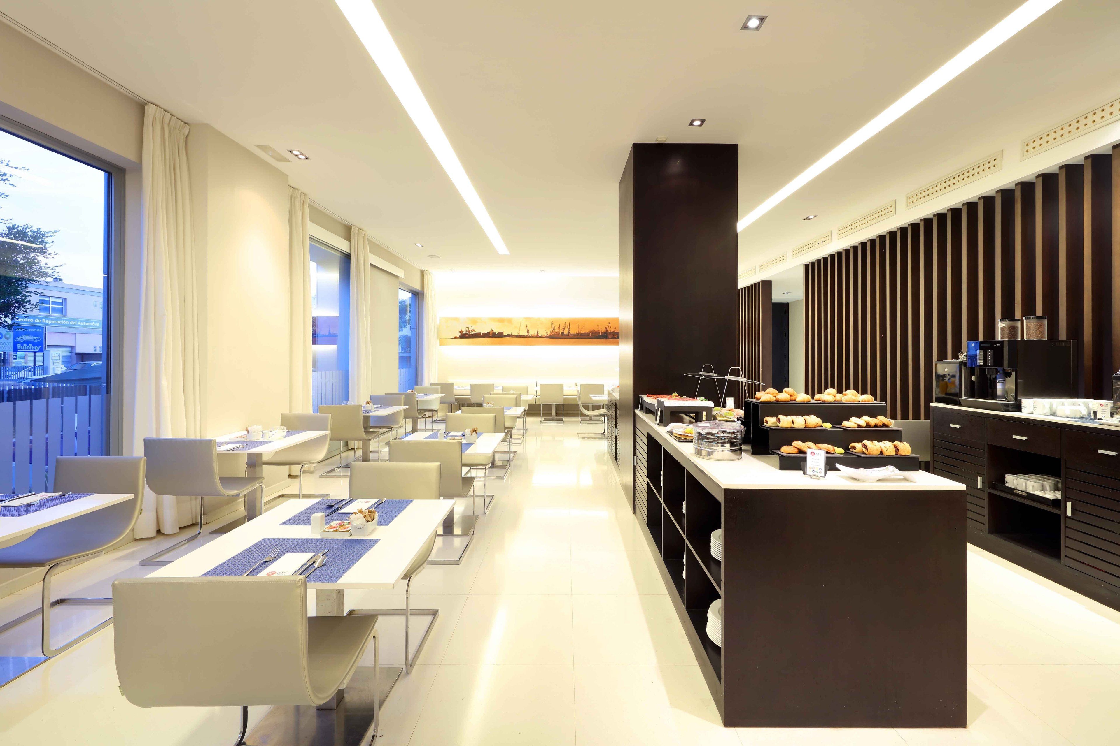 Comedor moderno de hotel con mesas largas, sillas y una isla central con pasteles.