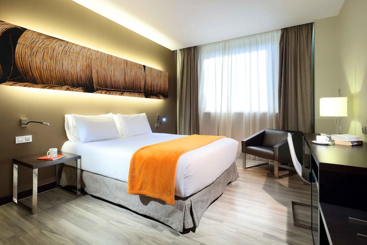 Ein Hotelzimmer mit einem großen Bett, einem Schreibtisch, einem Sessel und einem an der Wand befestigten Fernseher.