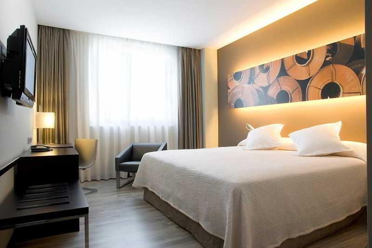 A hotel room with a bed, a desk, a chair, a TV, and a wall art piece.