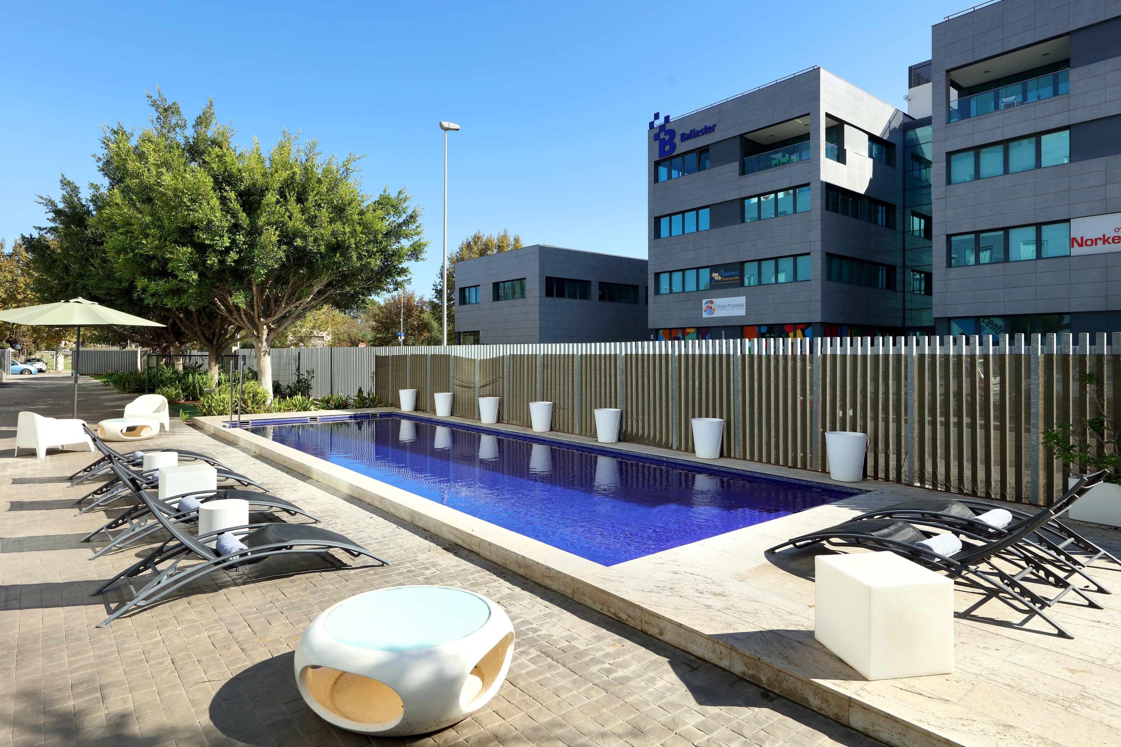 A swimming pool with lounge chairs and a small round table, surrounded by a wooden fence.