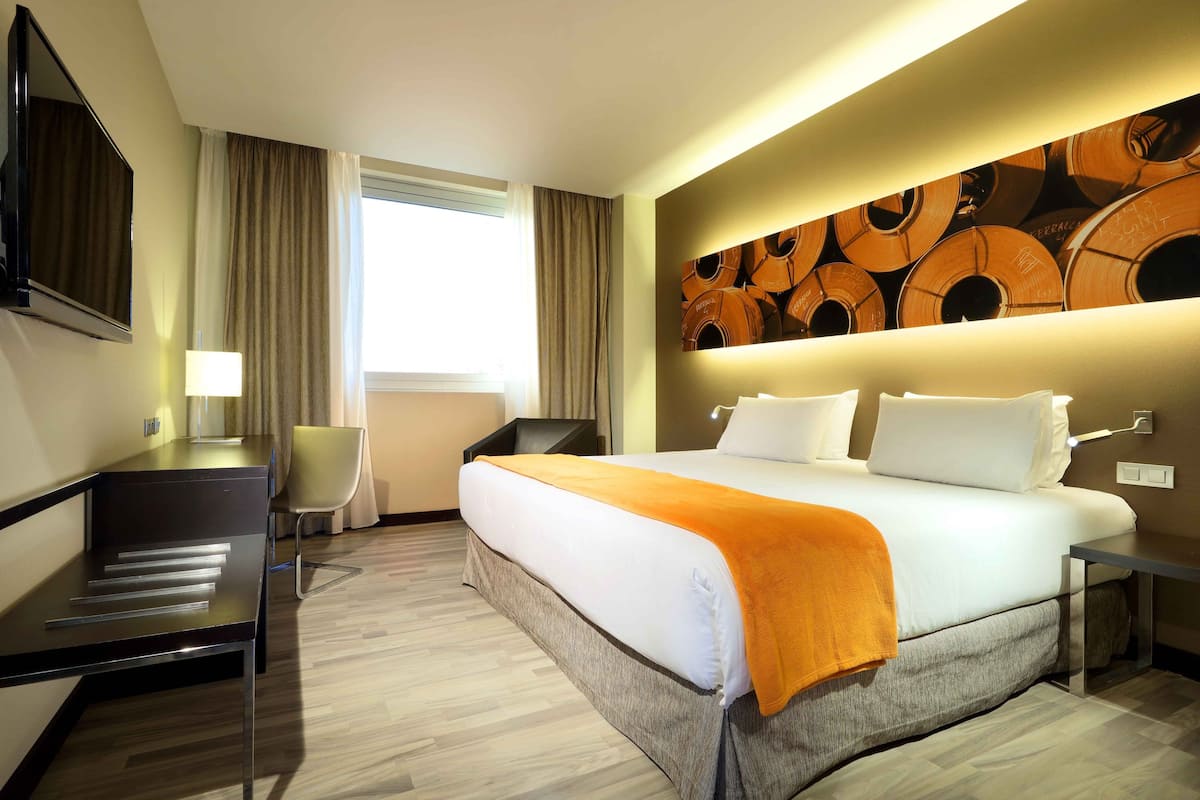Ein Hotelzimmer mit Bett, Schreibtisch, Stuhl, Fernseher und einer Wand mit einem gemusterten Design.