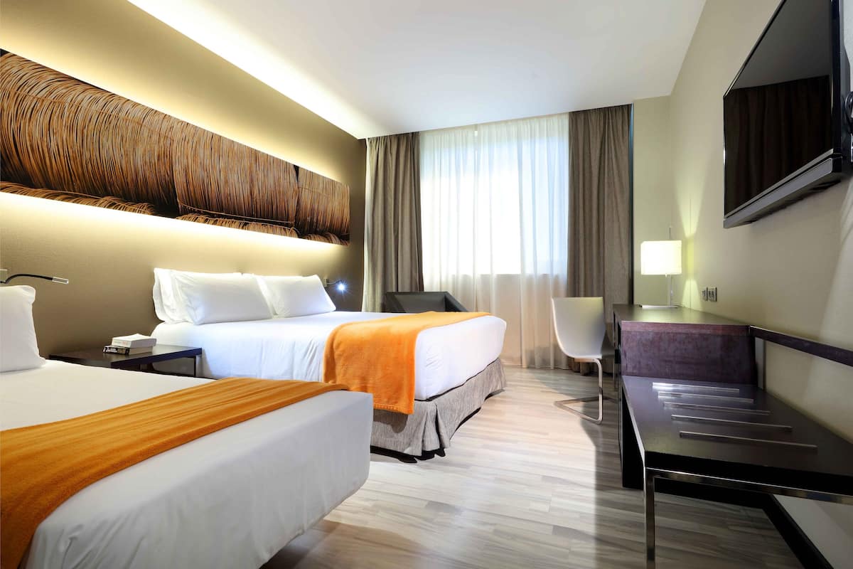 Ein Hotelzimmer mit zwei Betten, einem Schreibtisch, einem Stuhl, einem Fernseher und einem großen Fenster mit Vorhängen.