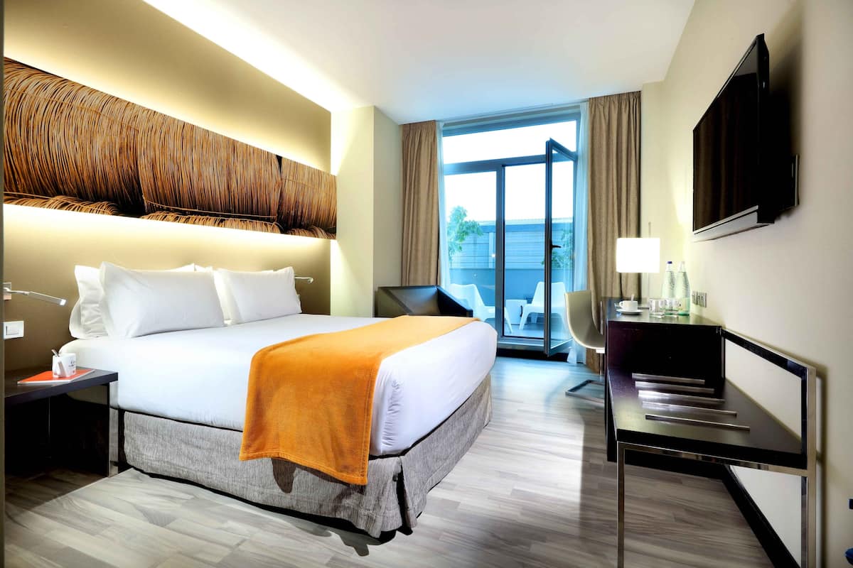 Ein modernes Hotelzimmer mit einem großen Bett, einem Schreibtisch, einem Flachbildfernseher und einem Balkon mit Aussicht.