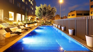 Una piscina con sillas de descanso y un árbol en el centro, rodeada de edificios con ventanas iluminadas.