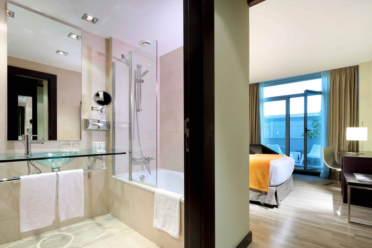 Ein modernes Badezimmer mit einer gläsernen Duschkabine, einem Glaswaschbecken und einem großen Spiegel. Das Zimmer verfügt über ein großes Fenster mit Blick ins Freie.