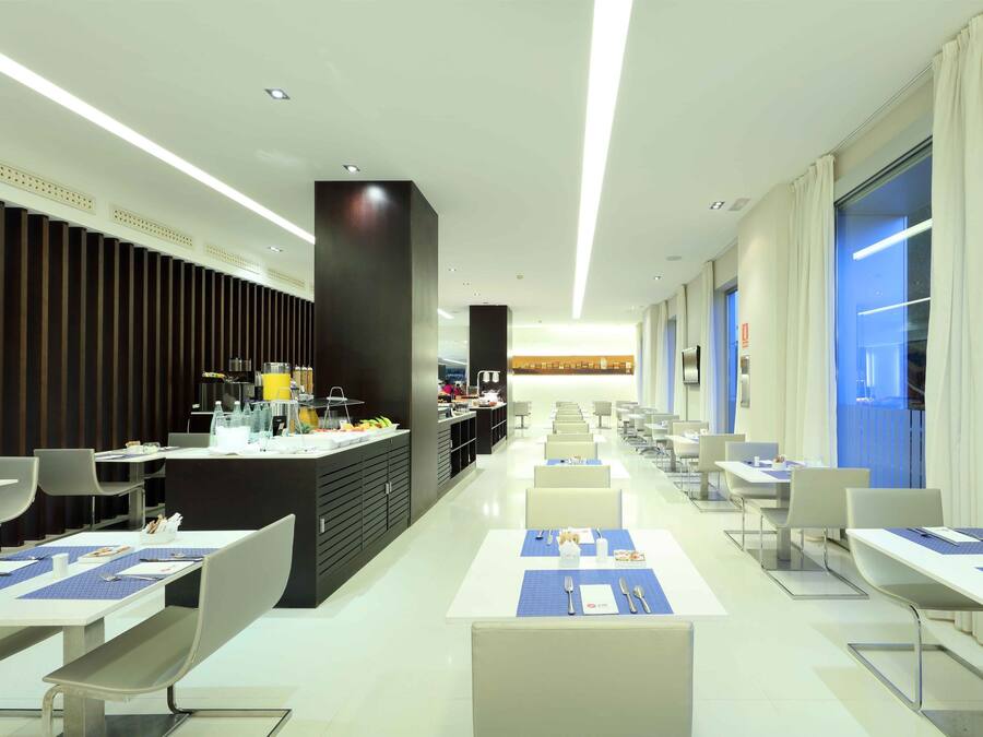 A modern dining area with long tables, chairs, and a central counter with various items.