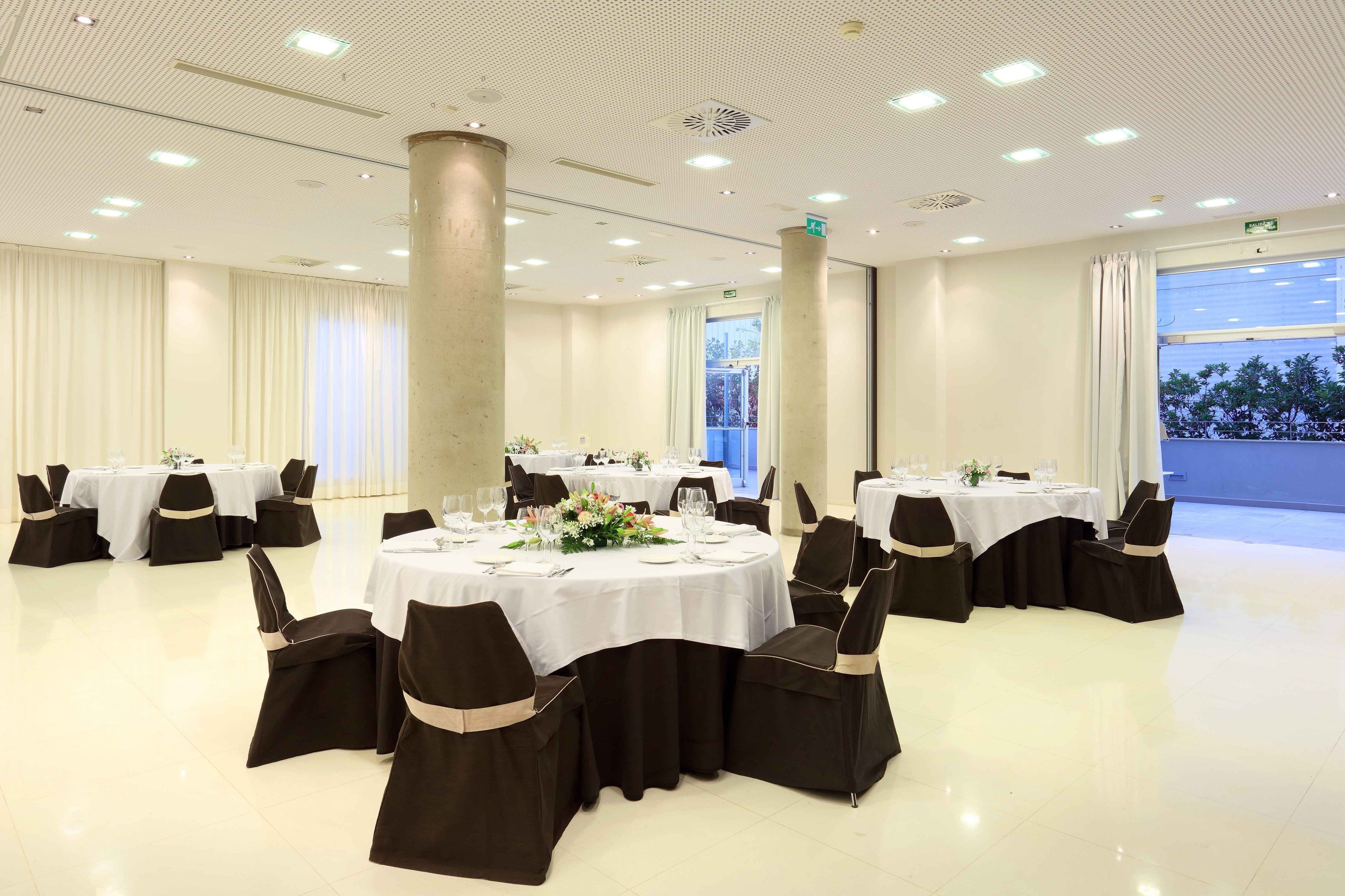 Un salón de banquetes con mesas redondas, sillas negras y manteles blancos.