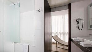 Un baño de hotel moderno con cabina de ducha de vidrio, un banco de madera y un tocador con teléfono.