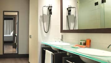 Een moderne badkamer met een glazen wastafel, een grote spiegel en een haardroger bevestigd aan de muur.