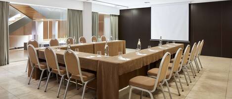 A conference room with a long table, chairs, and a projector screen.