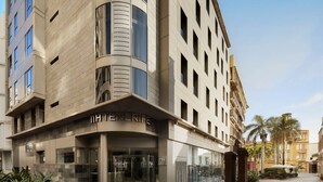 A modern hotel with a curved facade, large glass entrance, and a well-maintained outdoor area with palm trees.