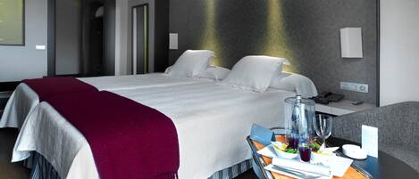 A modern hotel room with a large bed, a bedside table with a glass container, and a tray with breakfast items.