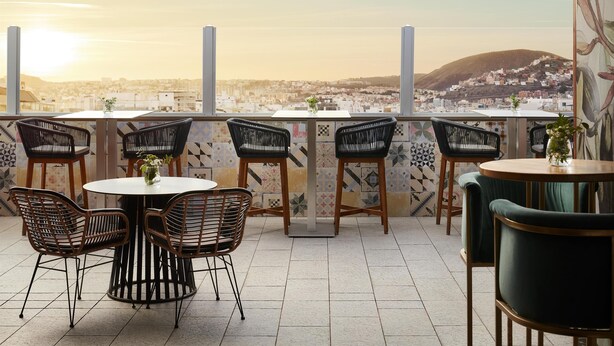 A terrace with round tables and chairs, a view of a cityscape, and a tiled floor.