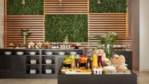 A buffet setup with various food items and drinks, wooden slats, and green foliage on the walls.