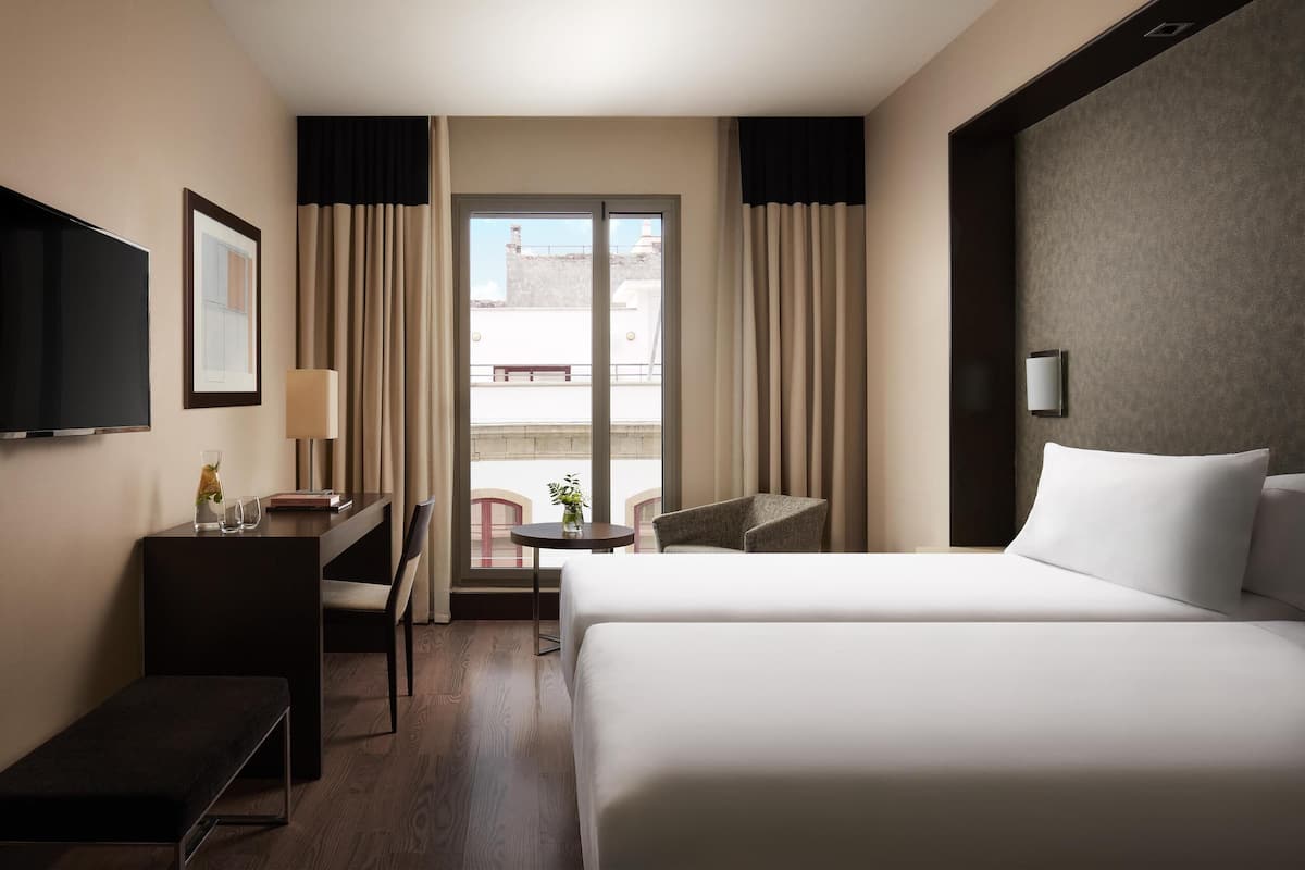 Une chambre d’hôtel avec un lit, un bureau avec une lampe, une chaise, une télévision et une vue sur l’extérieur.