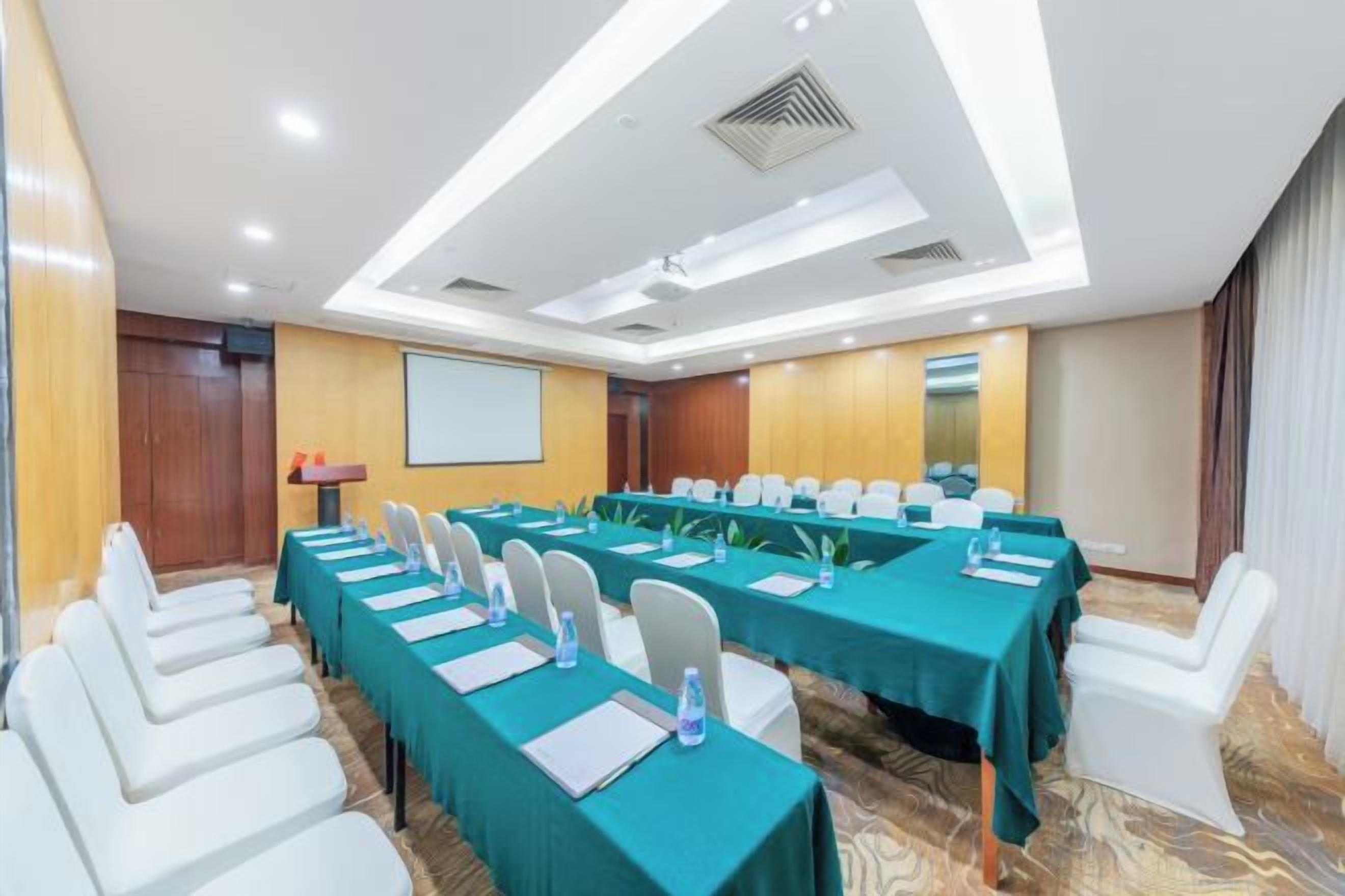 A conference room with long tables, chairs, and a projector screen.