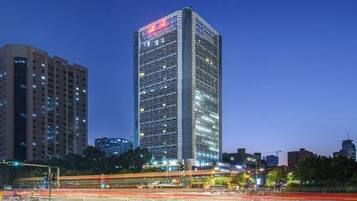 A high-rise building with a grid-like facade, surrounded by other buildings and a busy street with light trails.
