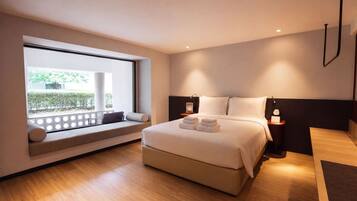 A modern bedroom with a large bed, a seating area by the window, and a view of greenery outside.