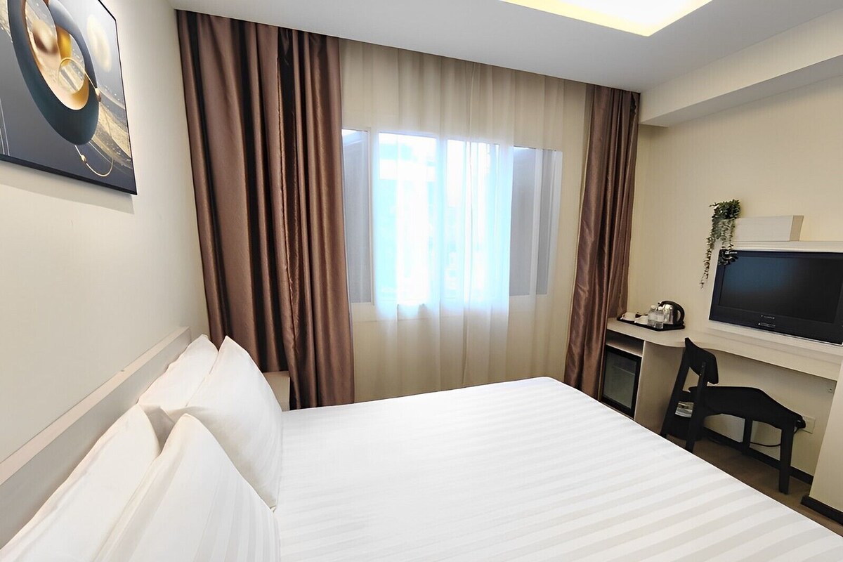 A hotel room with a bed, a desk with a television, and curtains.