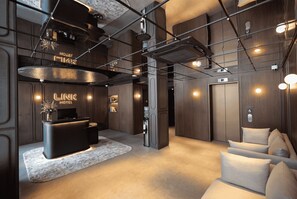 A modern hotel lobby with a reception desk, a water dispenser, and a seating area with cushions. - Link Hotel (Singapore)