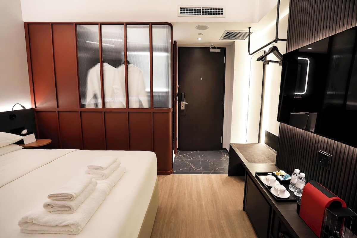 Habitación de hotel con cama, escritorio con bandeja de artículos de aseo, armario y puerta que da a otra habitación.