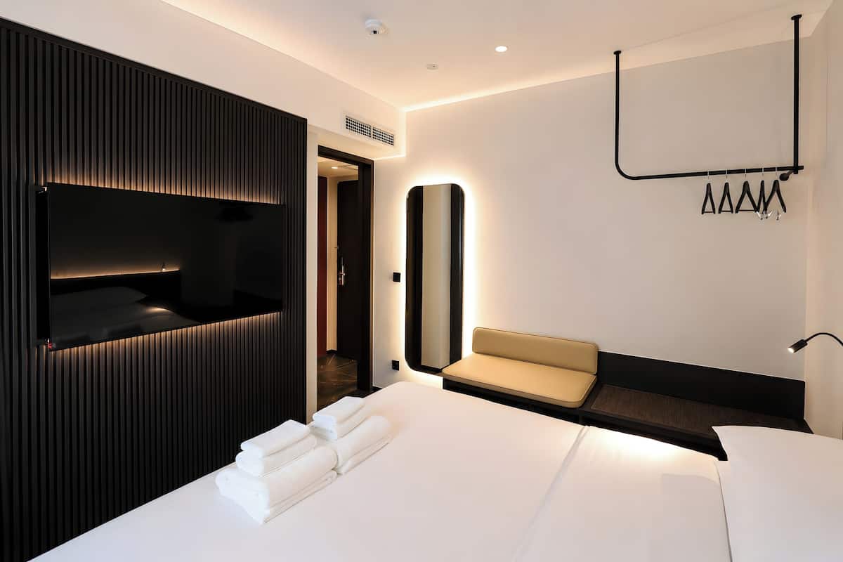 Una habitación de hotel moderna con una cama, un área de descanso, un televisor montado en la pared y un espejo.