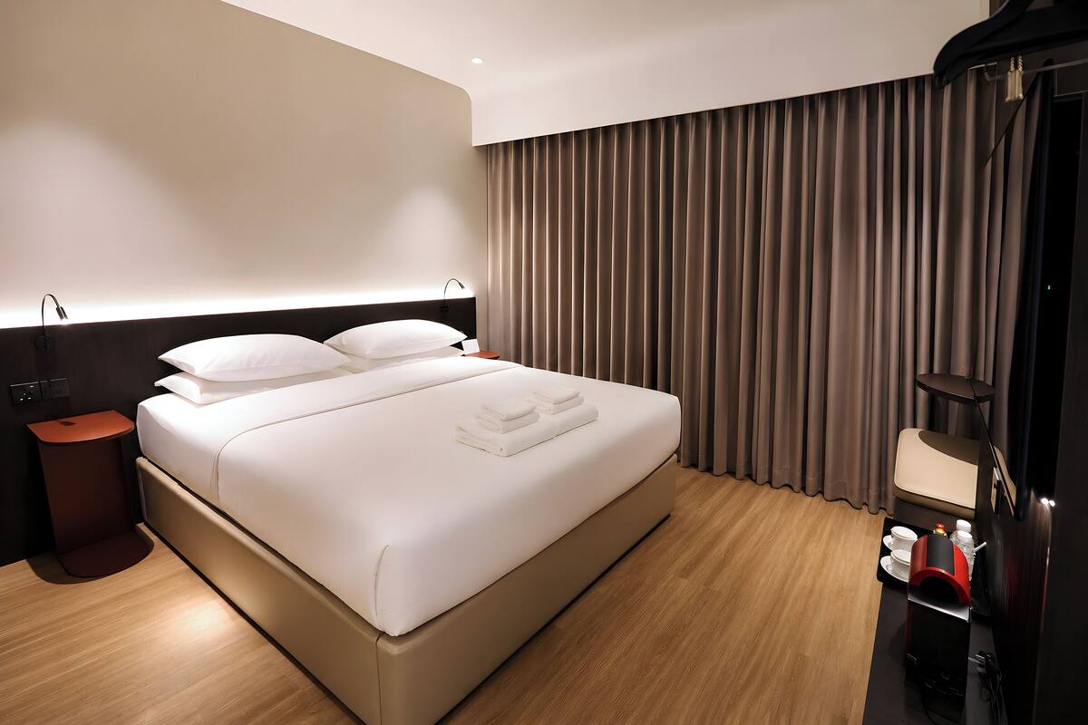 Una habitación de hotel moderna con una cama grande, una mesita de noche y un televisor integrado.