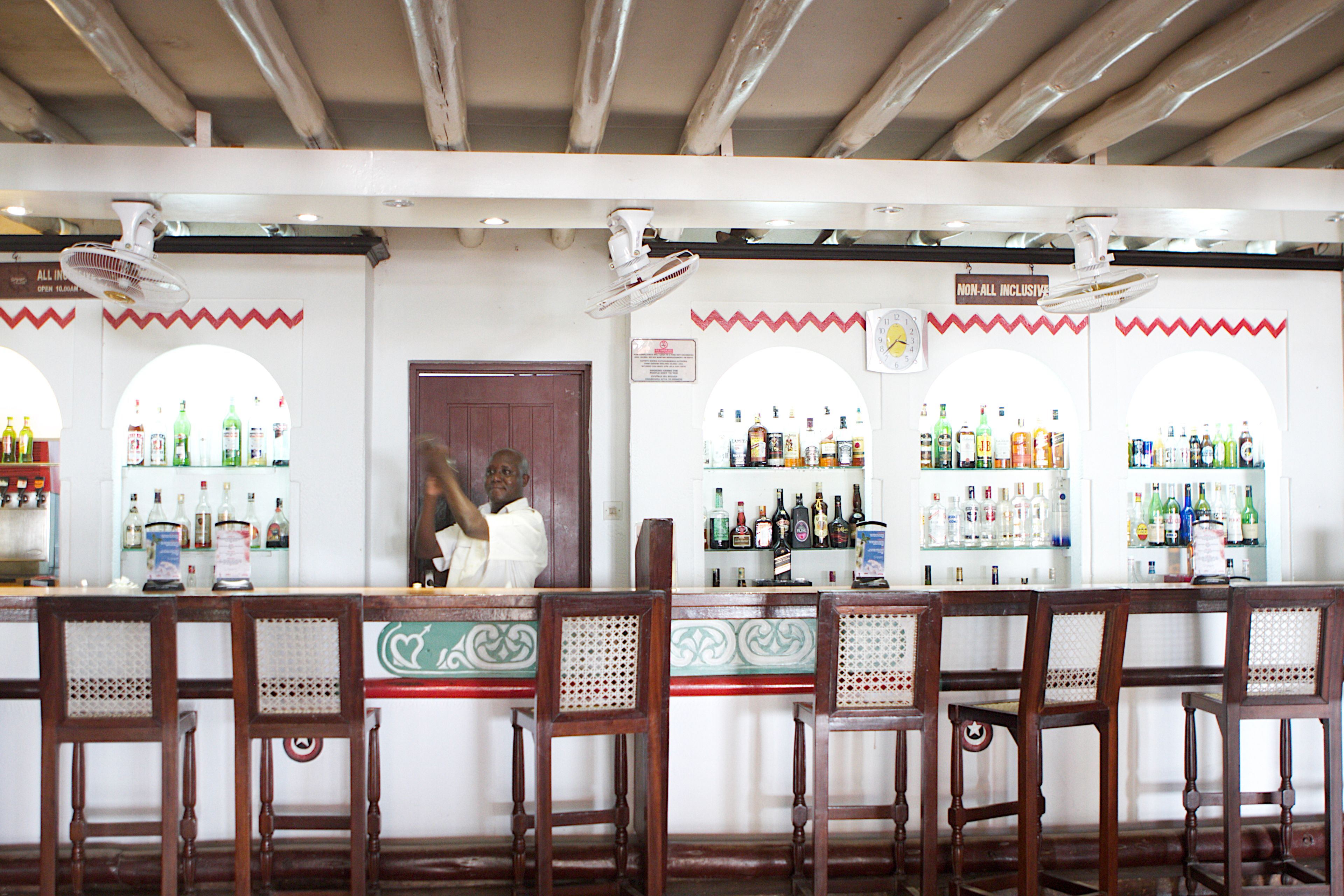 A bar with wooden chairs and a counter displaying various bottles.