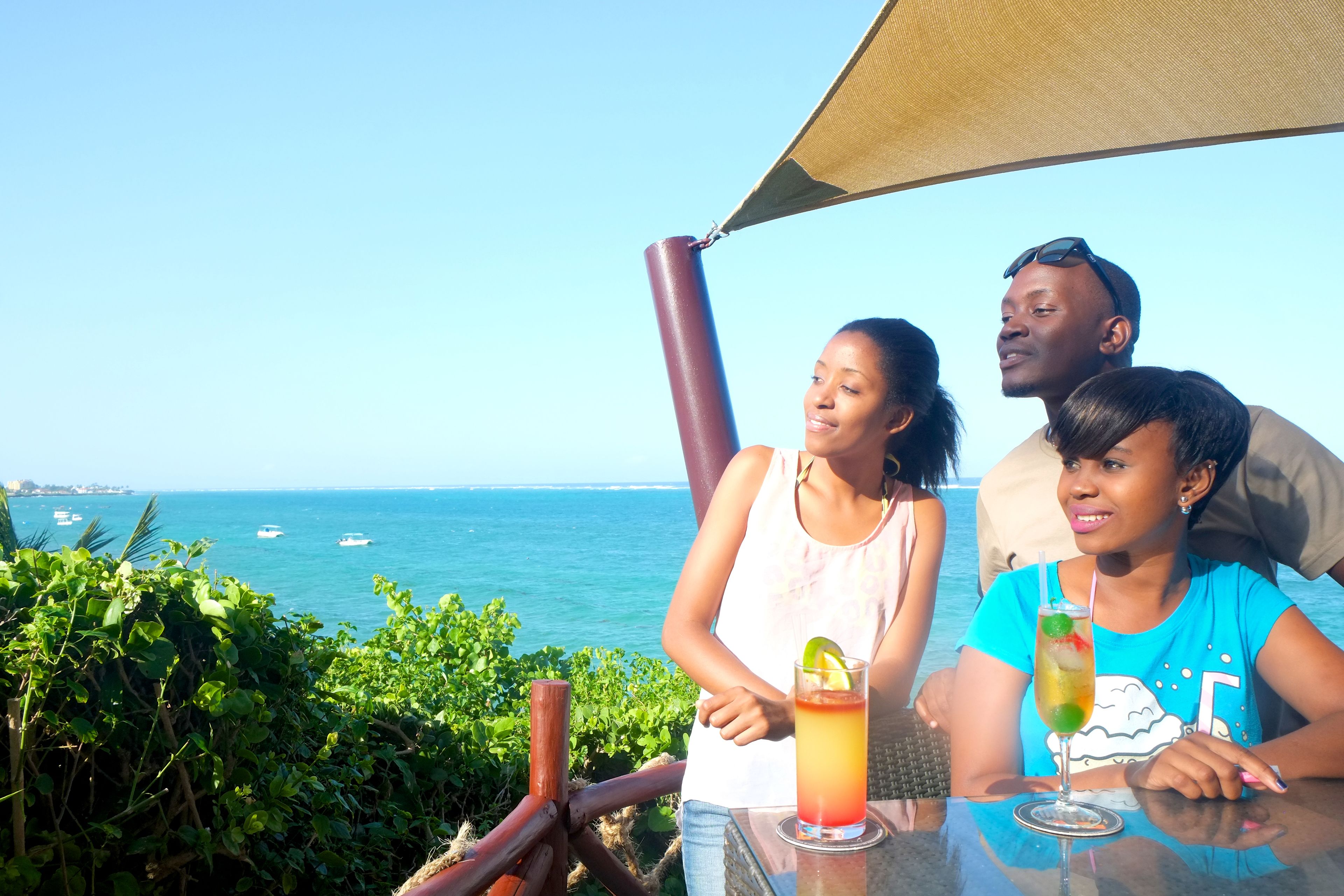 A group of people sitting at a table with drinks, overlooking a coastal view with boats in the distance.