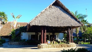 A thatched-roof structure with a stone base, surrounded by palm trees and a clear blue sky. - Voyager Beach Resort (Mombasa)