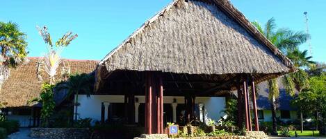 A thatched-roof structure with a stone base, surrounded by palm trees and a clear blue sky.