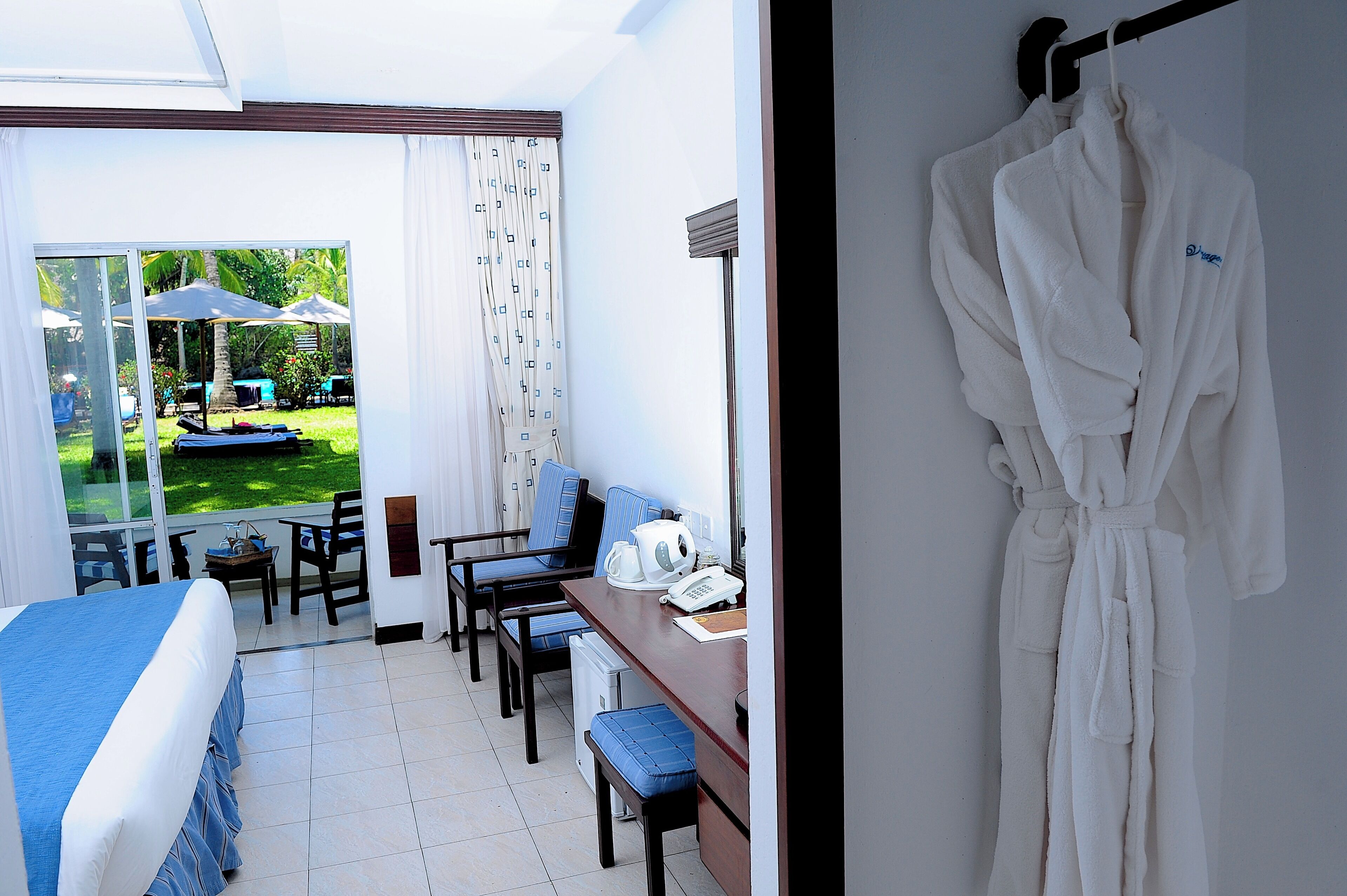 Habitación de hotel con cama, escritorio, silla, bata colgada en la pared y vistas al jardín.