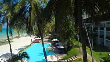 A pool area with lounge chairs and umbrellas, surrounded by palm trees and a view of the beach.