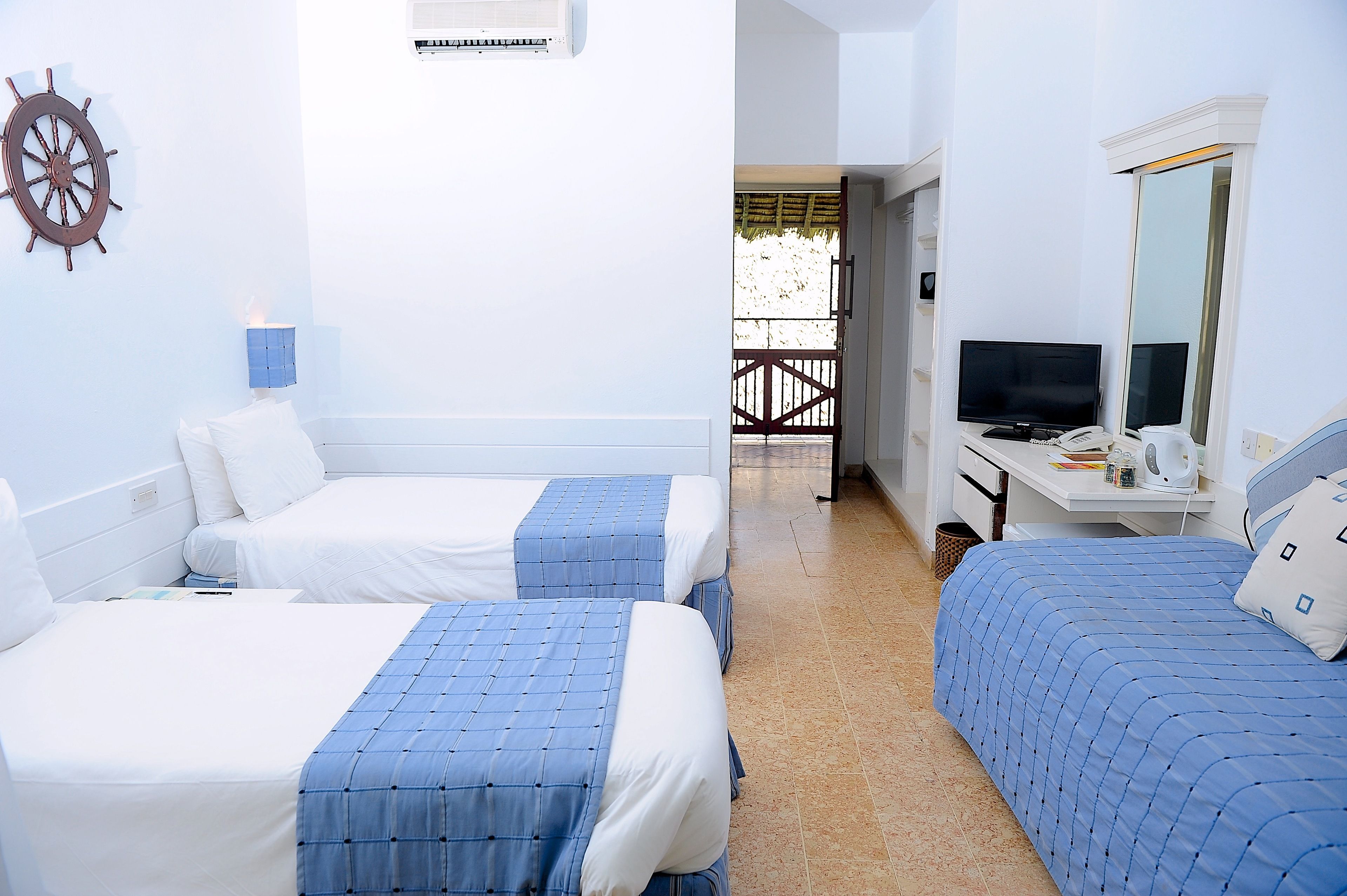A hotel room with two beds, a desk with a computer and phone, a TV, and a large mirror.