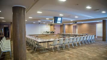 Una sala conferenze con diverse tavole e sedie, un ampio pilastro e uno schermo televisivo a soffitto.