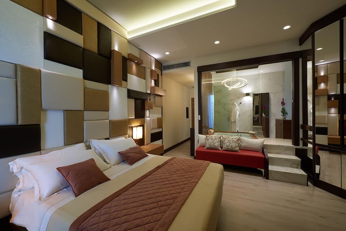 Een moderne hotelkamer met een groot bed, een rode bank en een spiegel die de badkamer weerspiegelt.