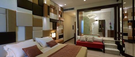 A modern hotel room with a large bed, a red sofa, and a mirror reflecting the bathroom.
