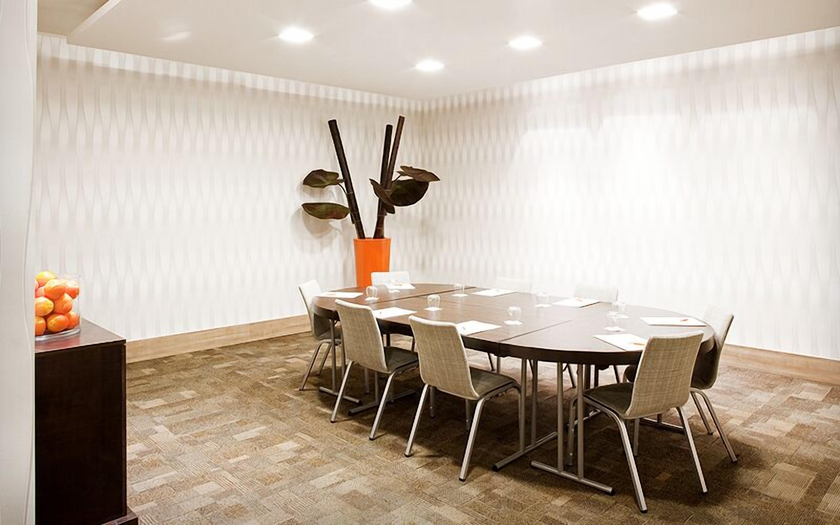 A conference room with a round table, six chairs, a vase with decorative sticks, and a fruit bowl on a side table.