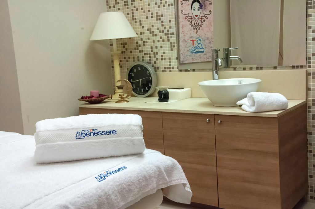 A hotel bathroom with a wooden vanity, a white sink, a clock, a mirror, and towels with a logo.