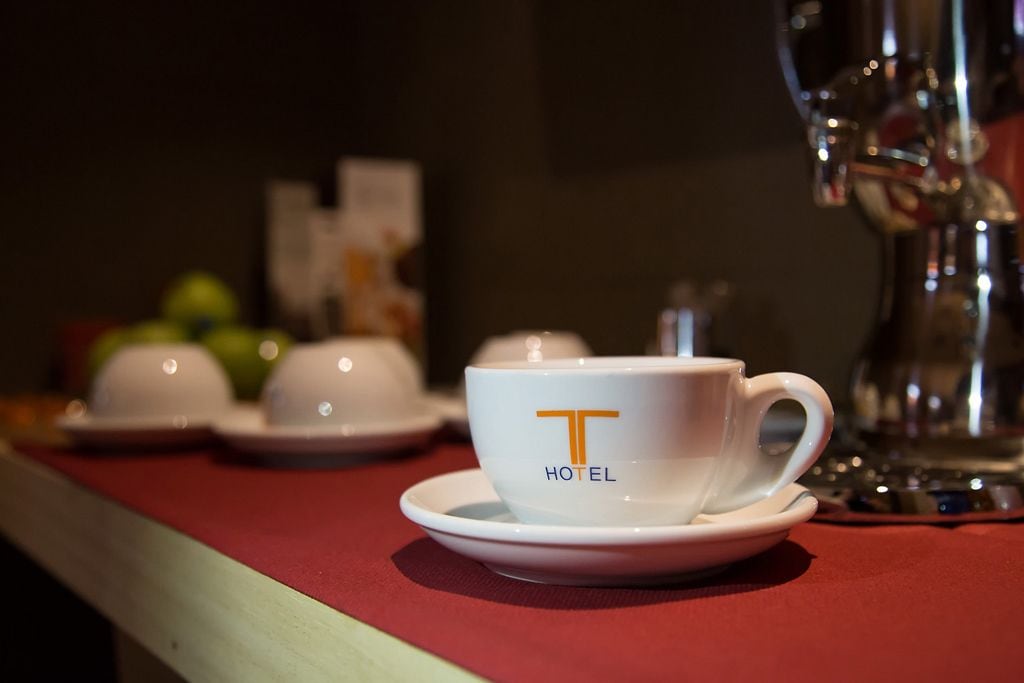 A white cup with a logo on a saucer, placed on a red table with a blurred background.