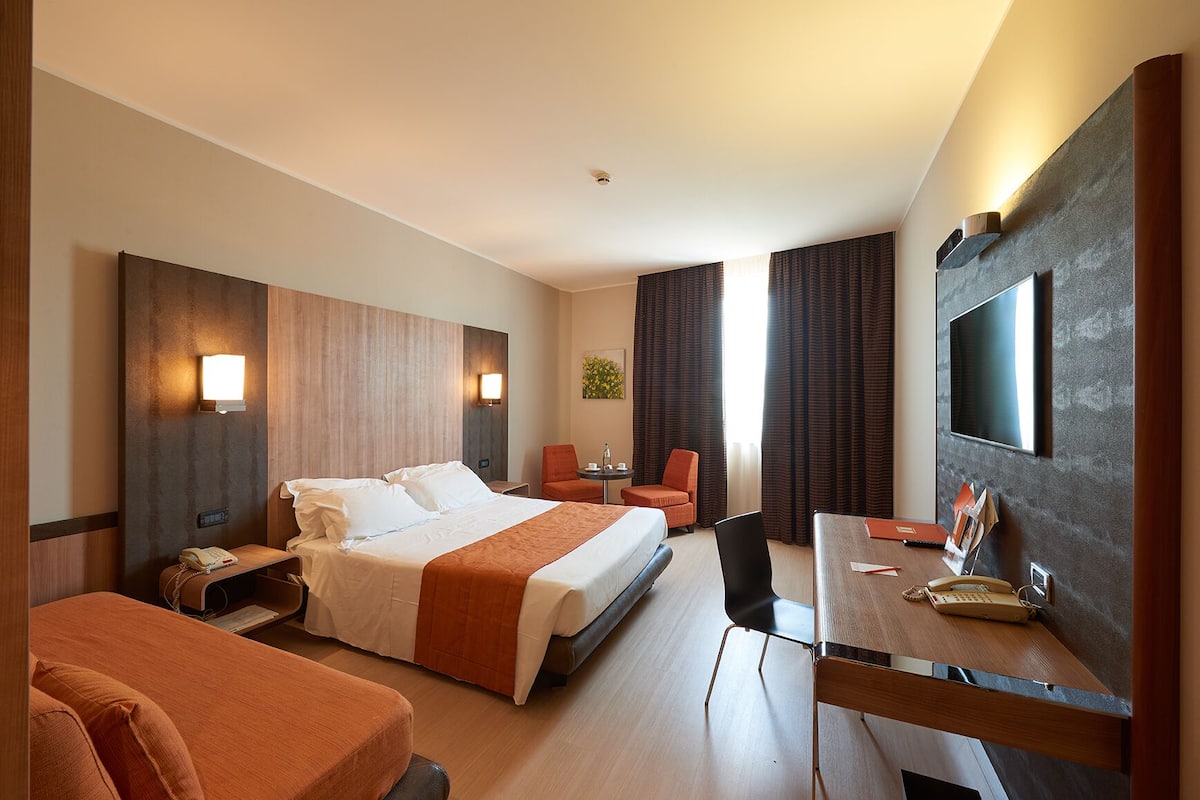 Een hotelkamer met een groot bed, een bureau, een stoel, een televisie en een kleine tafel met een lamp.