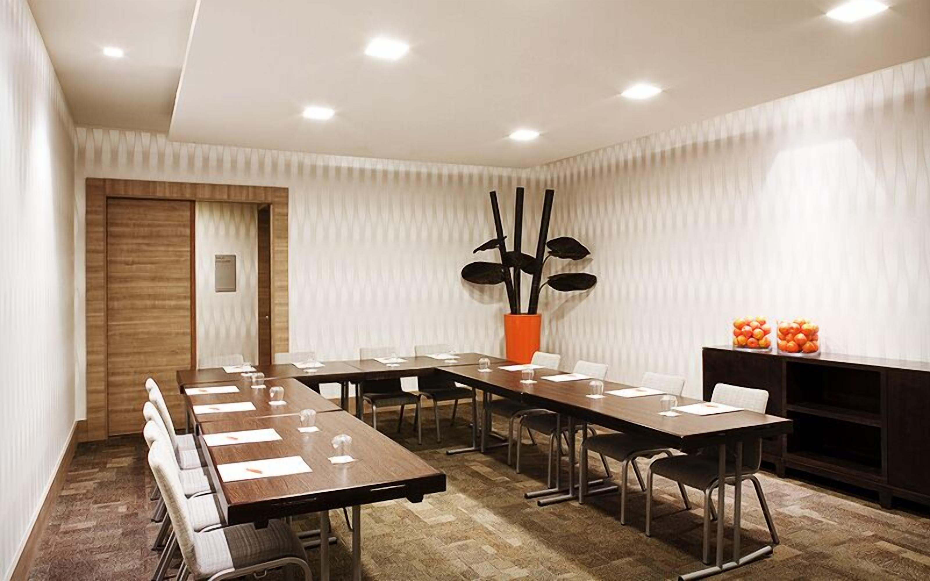 A modern conference room with a long table, chairs, a potted plant, and a fruit display.