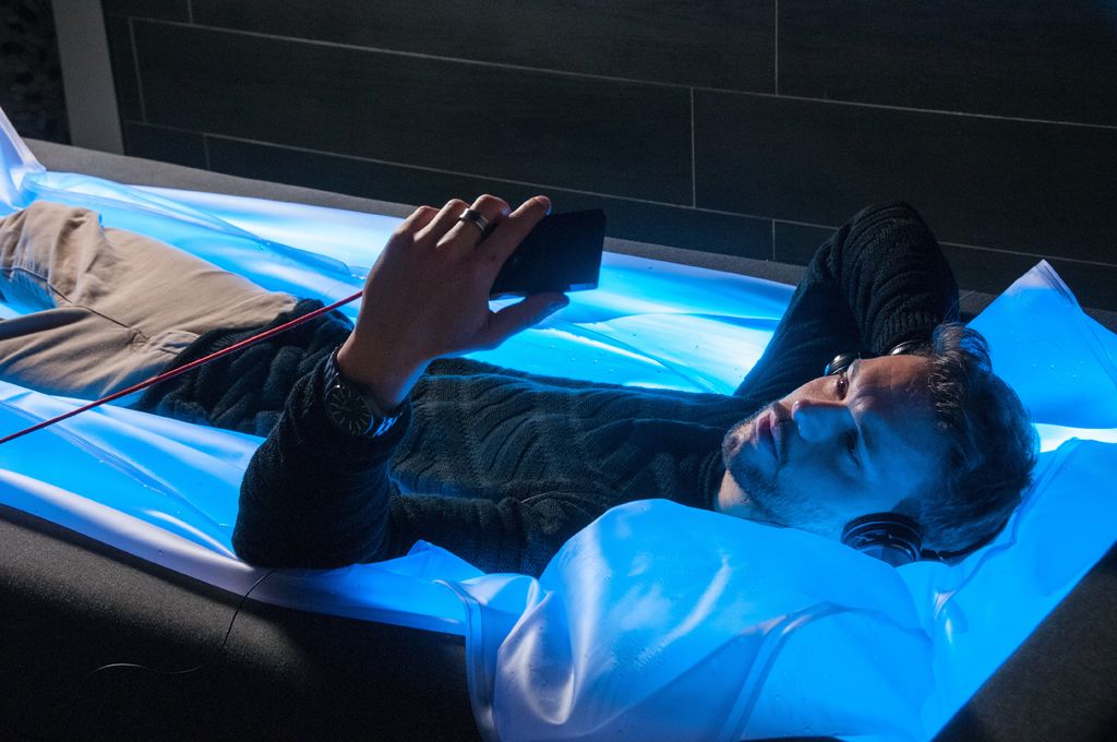 A person lying on a bed with a blue light, holding a smartphone.