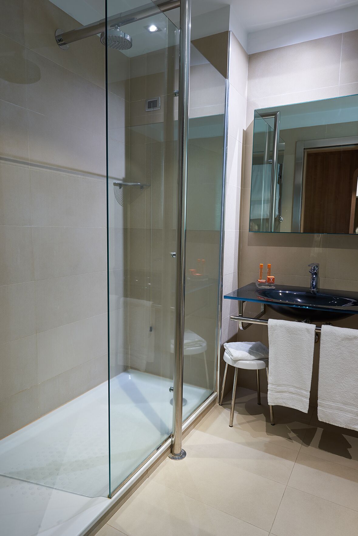 A modern bathroom with a glass-enclosed shower, a glass-topped vanity, and a white toilet.