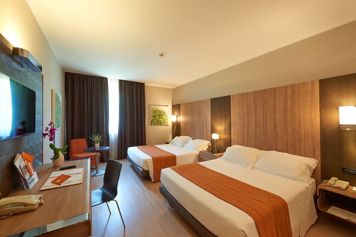 Een hotelkamer met twee bedden, een bureau met telefoon, een stoel en een kleine tafel met een plant.