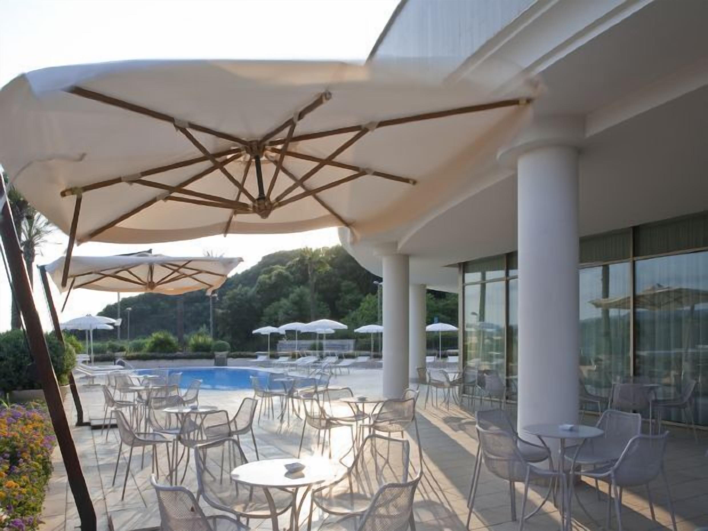An outdoor seating area with tables and chairs, umbrellas, and a pool in the background.