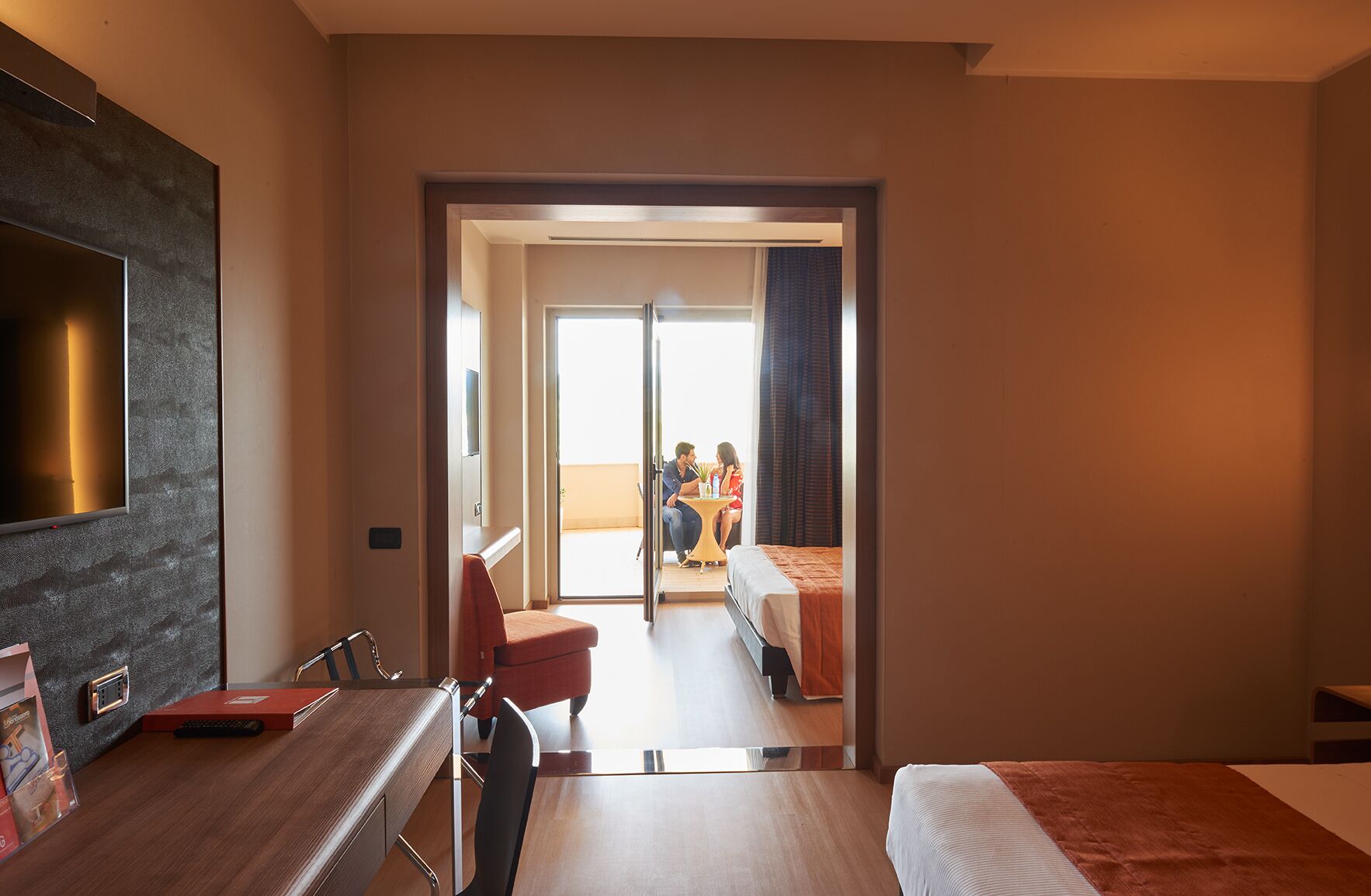 Une chambre d’hôtel équipée d’un bureau, d’une chaise, d’un lit et d’un téléviseur fixé au mur.