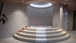 Une structure circulaire en pierre, composée de plusieurs niveaux, avec un luminaire central, le tout entouré d’un mur à la texture particulière.